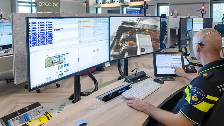 Politieagent kijkt op meldkamer naar twee schermen, waarvan 1 WeSeeDo laat zien